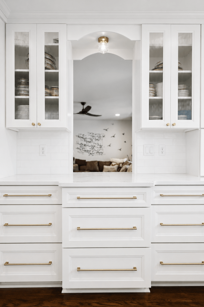 A transitional-style kitchen passthrough with arched opening, reeded glass cabinetry, brushed brass hardware, and white quartz countertops — designed by Jacksonville interior designer Emily Cornaire of San Marco Art and Design